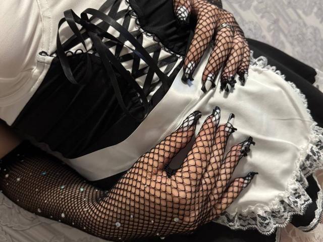 FallenAngelia's hands with black fishnet gloves and long, sharp, black-and-white manicured nails resting on a black-and-white corset and white apron with lace.