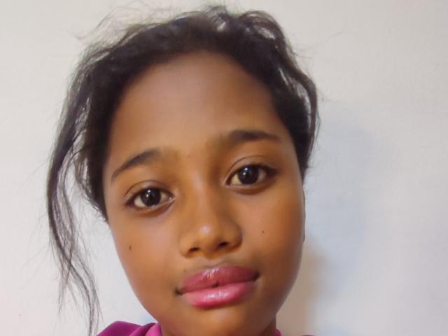 BetyBoobs has dark brown skin, black curly hair, brown eyes, small nose, and pink glossy lips. Her face is centered, looking slightly to the left.