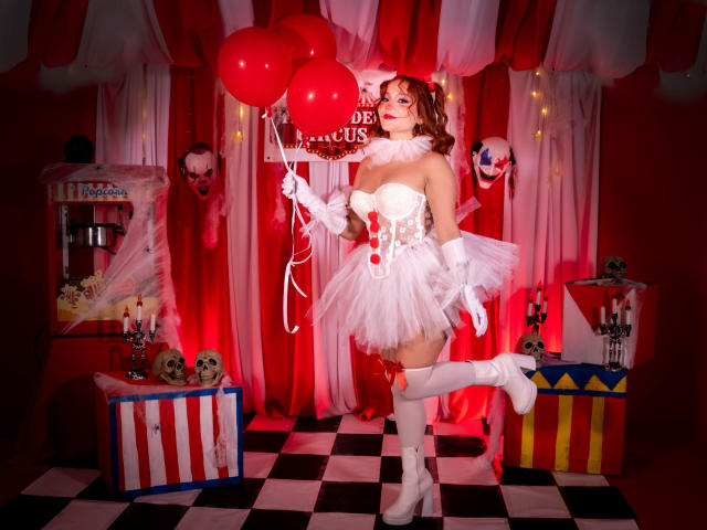 EmilyKlein with red balloons, white strapless dress, fluffy tutu, white gloves, thigh-high boots, holding a sign, surrounded by clown masks and gift boxes, standing on checkered floor.