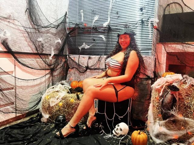 AshleyJenner, avec ses longs cheveux noirs et sa casquette noire, est assise sur une balle de foin, en maillot de bain rayé, montrant ses fesses et ses seins, entourée de décorations d'Halloween..
