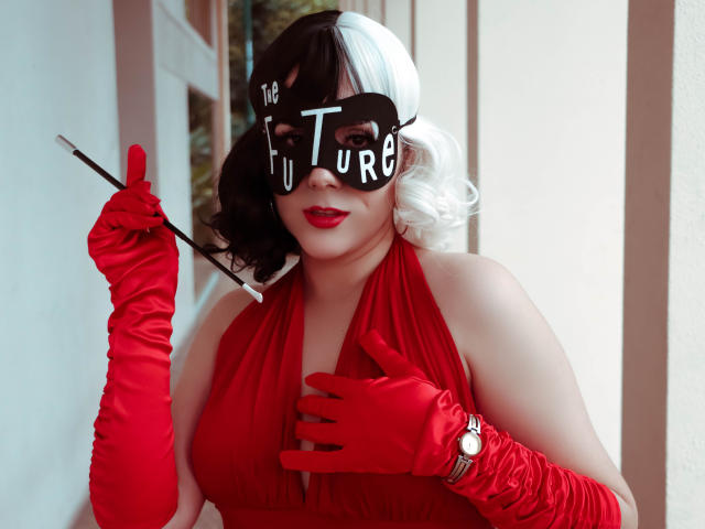 GoddessBar with white and black curly hair, red dress, and gloves, holding a stick, wearing a black mask with "The Future" in white, red lipstick, touching chest.