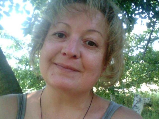 ClaraPink a les cheveux blonds courts et en désordre, et un petit sourire. Elle porte un débardeur gris et une chaîne, et se trouve dans un environnement extérieur ensoleillé. Ses seins sont légèrement visibles..