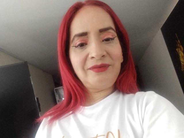 Kate Monroe, con i capelli rossi, l'ombretto rosa e il rossetto rosso, sorride, indossa una camicia bianca, mostrando un viso carino e tratti delicati..