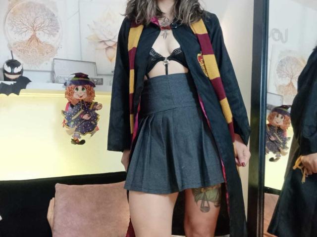 ArianaBlonde wears a black open robe with yellow stripes, black lace bra, and gray pleated skirt, showing her tits and a tattoo on her thigh.