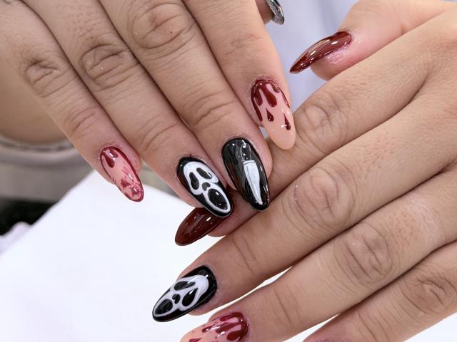NatalieHarris's hands with glossy, marbled nails—red, black, and white with flame patterns. Her fingers are slightly curled, showcasing sharp, dark red and black nails.