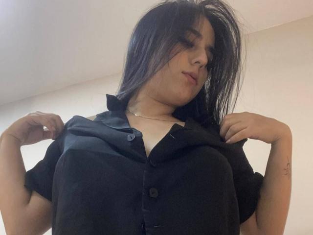 StefanyDelly with dark hair, wearing an open black shirt, showing her large tits, hands on shirt edges, slightly messy hair, light skin, subtle tattoo on right wrist.