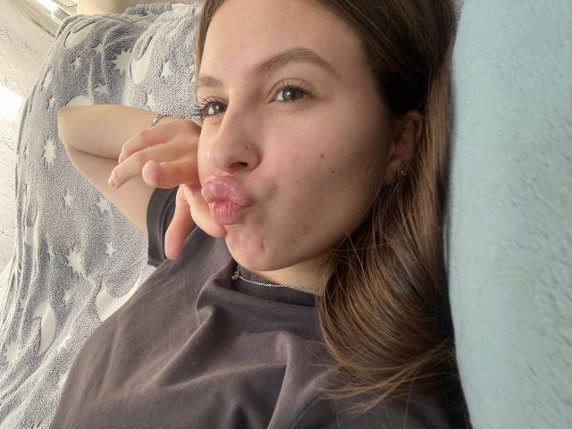 Audrie Nuessen, met volgezwollen lippen, bruin haar, een zwart shirt, een neusring en lichte huid, maakt een kusgezicht en ligt op een blauw kussen..