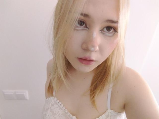 AnnieLeonhart69 with blonde hair, white lace bra, and a slightly dazed expression, has a white liquid on her face and lips, and a light skin tone.