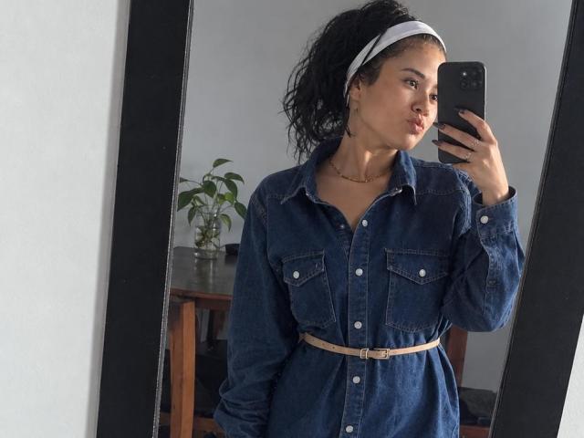 IsabellaVoss in a denim dress with pockets, white headband, and beige belt, taking a mirror selfie with her phone, showing her ass and pouty lips.