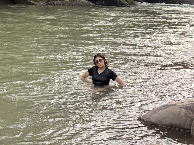 Laniita's dark wet hair clings to her face as she stands in a river, wearing a black Nike shirt, with her tits and ass just above the water's surface.