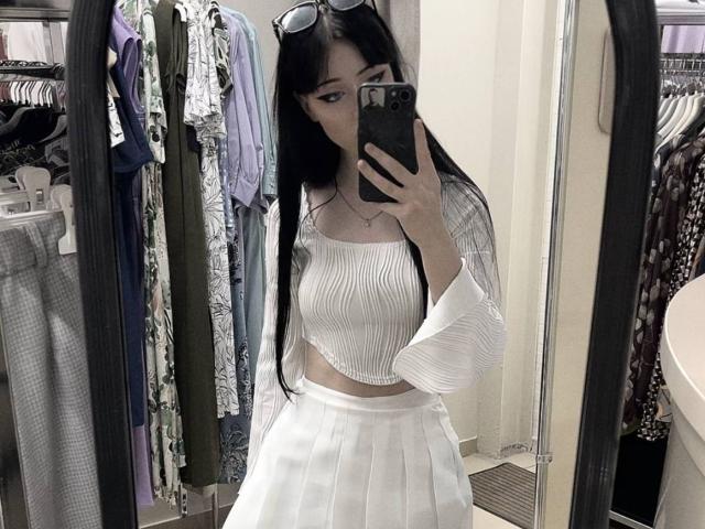 KiraLowkey with long black hair, wearing a white ribbed crop top and high-waisted white skirt, taking a mirror selfie with her phone, showing her tits and ass.