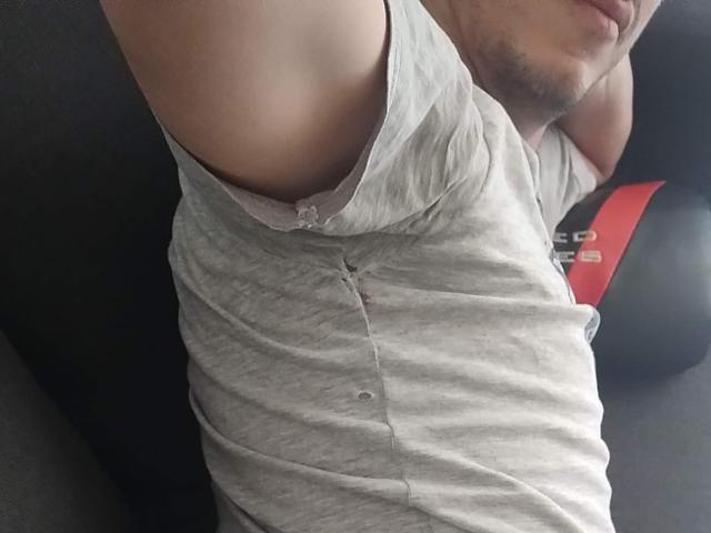 A camisa cinza de XSantyX está ligeiramente levantada, revelando um pequeno rasgo e uma alça de sutiã branca por baixo da camisa. O braço de XSantyX está levantado, parcialmente visível à esquerda..