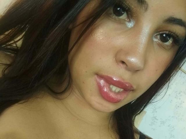 AndreaAleman's face, showing shiny skin, dark brown eyes, glossy pink lips, and long black hair. Her nose is centered, with a slight smile and visible teeth.