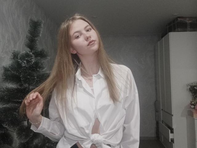 MargretWarriner with long blonde hair, wearing a white button-up shirt tied at the front, holding her hair, standing in front of a decorated Christmas tree.