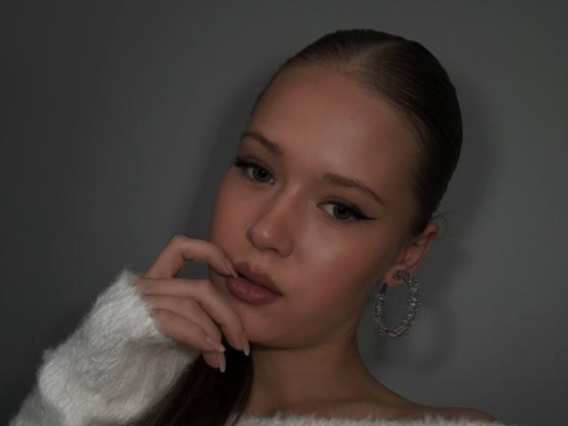 LillianaWhang with a cute face, wearing a white fuzzy sweater, has her finger near her mouth, sporting hoop earrings, and looking at the camera with a subtle smile.