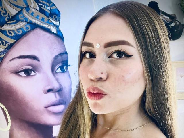 AlessiaCruz has brown hair, a nose ring, and a forehead gem. She's next to a purple-tinted, black-and-white portrait of a woman with a blue headscarf and earrings.