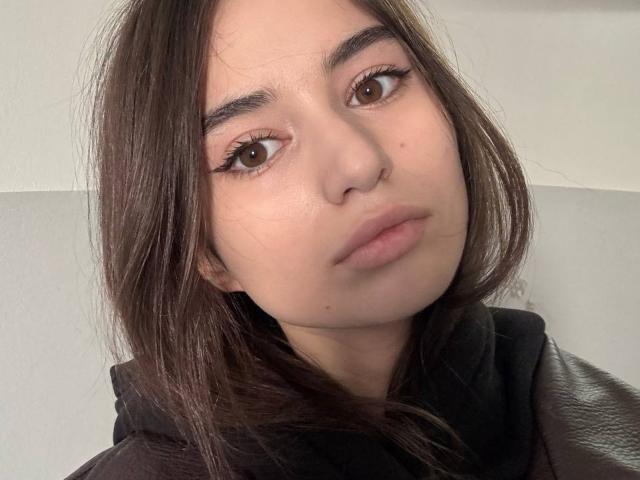 TonetteMatheu a les yeux marron, des sourcils épais et les cheveux bruns et lisses. Elle porte un sweat à capuche noir et a l'air sérieuse, avec les lèvres légèrement pincées. Sa peau est claire et lisse..