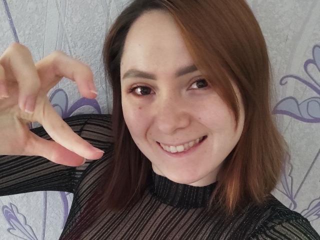 Patricia Casgrove, de piel clara, cabello castaño, sonriendo, vestida con una blusa negra transparente, señalando con su mano derecha, mostrando sus dedos con uñas rosadas, y con sus pequeños senos visibles..