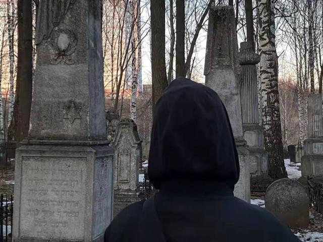 MariannaWarren with a black hoodie, facing a bunch of old, grey tombstones in a snow-covered, leafless cemetery, standing with her back to the camera.