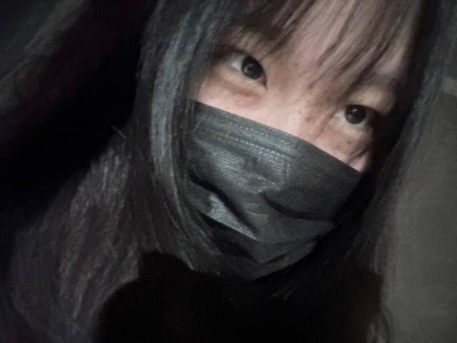 JungMcgranor with greyish-black mask covering nose and mouth, greyish-black hair, and intense eyes looking forward, dark shadowed face, photo has a gritty, low-light feel.