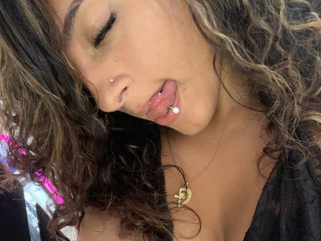 CristalAndRichard a les cheveux bruns bouclés, une peau mate, un piercing au nez et un piercing à la langue avec une petite bille blanche. Elle lèche sa lèvre inférieure les yeux fermés..