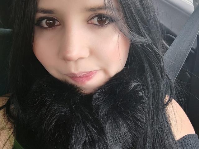 Kkatalina, met zwart haar, bruine ogen en bleke huid, draagt een zwarte bontsja en zit in een auto. Ze heeft een lichte glimlach en een schattig, aantrekkelijk gezicht..