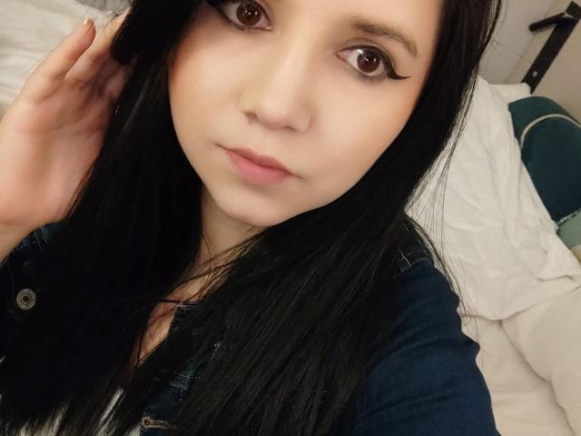 Kkatalina mit langem, schwarzem Haar, braunen Augen und dezentem Make-up, trägt ein Jeanshemd und hat einen ruhigen Gesichtsausdruck. Ihre Hand berührt ihren Kopf in einem Selfie..