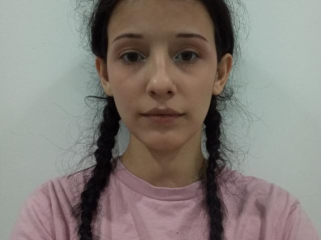 Concepcion Rhynard, con trenzas negras, camisa rosa, aro en la nariz y una sonrisa sutil, mirando directamente a la cámara con los labios ligeramente entreabiertos, mostrando pequeños senos y un rostro lindo..