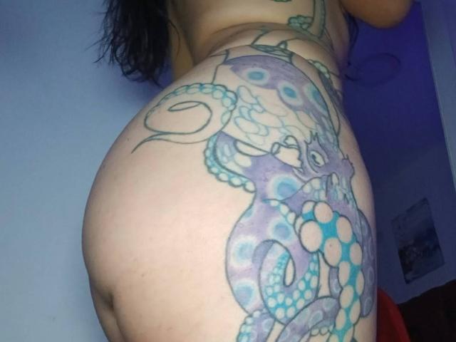 Les fesses tatouées de ZarayFeet arborent un motif d'un poulpe détaillé et coloré, avec des motifs bleus et violets, qui s'enroulent autour de leur côté droit et de la partie supérieure de leurs fesses..