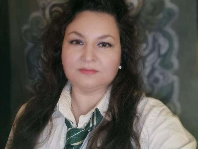 DivineElla a les cheveux bouclés, d'un brun foncé, des yeux marron et un visage légèrement rond. Elle porte une cravate rayée verte avec une chemise blanche, et de petites boucles d'oreilles..