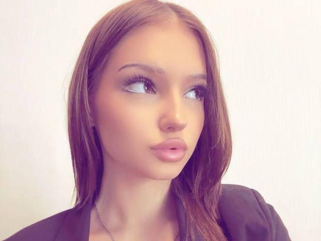 ShanekaKonig has brown hair, pouty pink lips, and a slightly upturned nose, looking to the side with a serious expression, wearing a black top.