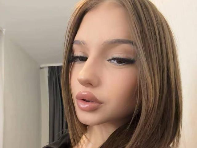 ShanekaKonig has glossy pink lips, long brown straight hair, and heavy black eyelashes. Her skin is smooth and tan, with a slightly open mouth. She's looking to the side.