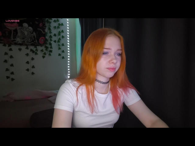 JessicaDigiorgio has orange-red hair, pale skin, and wears a white tee with a black choker. She's looking to the side with a slight smile, showing pink lips.