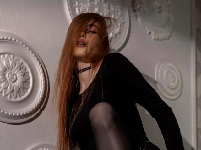 MargoKoli with long brown hair, black top, and black tights, has her face tilted up, eyes closed, and mouth slightly open, showing her small tits and black choker.