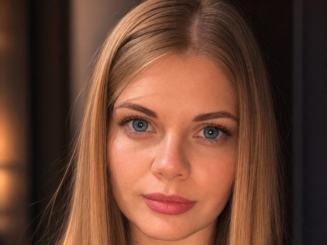 Pannia has straight blonde hair, blue eyes, and pink lips. She's staring with a serious, slightly smug expression. Her tits aren't visible. She's attractive and has a cute face.