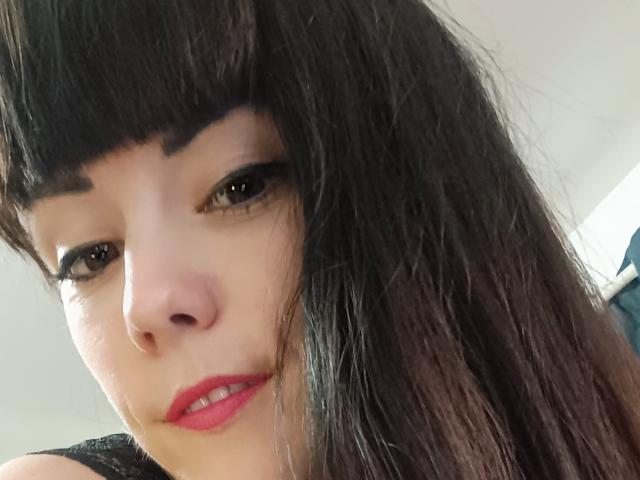OrianaLaFrancaise's Gesicht mit dunklem, gewelltem Haar, dicken, schwarzen Augenbrauen, braunen Augen, rotem Lippenstift und einem subtilen Lächeln, das einen süßen, sexy Look zeigt. Ihre Nase ist klein und niedlich..