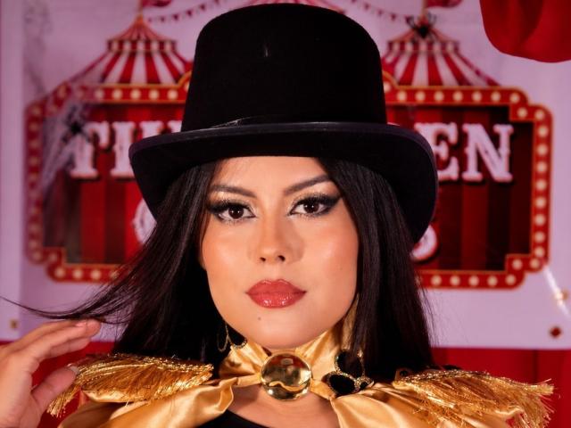 ElectraRoss, met glanzende rode lippen, donkere ogen en een zwarte hoed, draagt een gouden choker en epauletten, heeft lang zwart haar en een zelfverzekerde uitdrukking. Borsten niet zichtbaar..