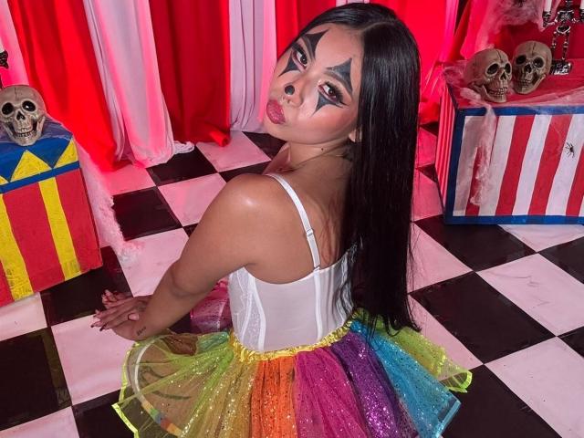ChloeMoretti with long black hair, white corset, colorful sparkly skirt, star makeup on face, pouty lips, kneeling on black and white checkered floor, surrounded by skulls and gifts.