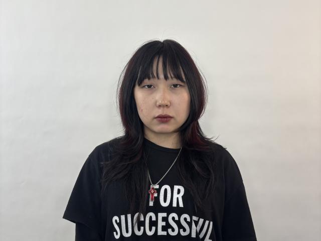 LorenzaKrzeminski, with dark, slightly wavy hair and a serious face, wears a black t-shirt, has a small nose ring, and a silver necklace with a red pendant.