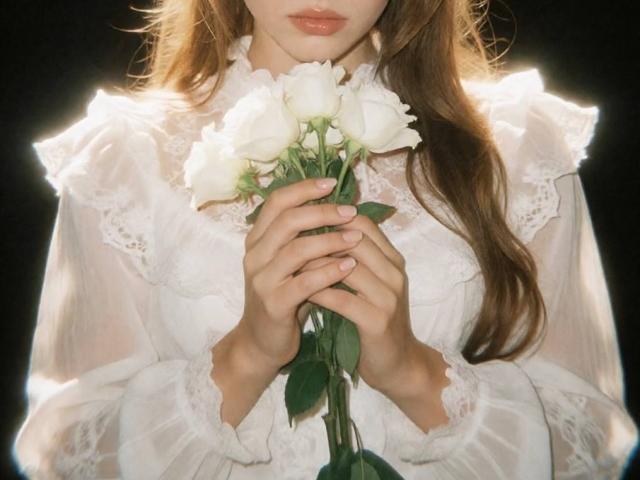 ViolletaMoon holding white roses with her delicate hands, wearing a sheer, lace-trimmed white dress, her long brown hair cascading over her shoulders.