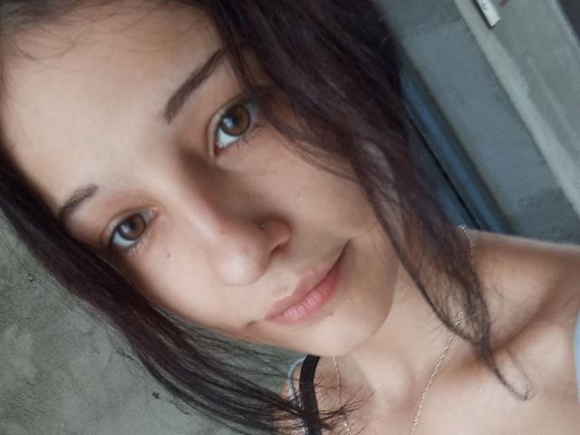 ConcepcionRhynard's face, showing brown eyes, a small nose piercing, and a subtle smile. She has dark, messy hair and wears a thin necklace with black straps.