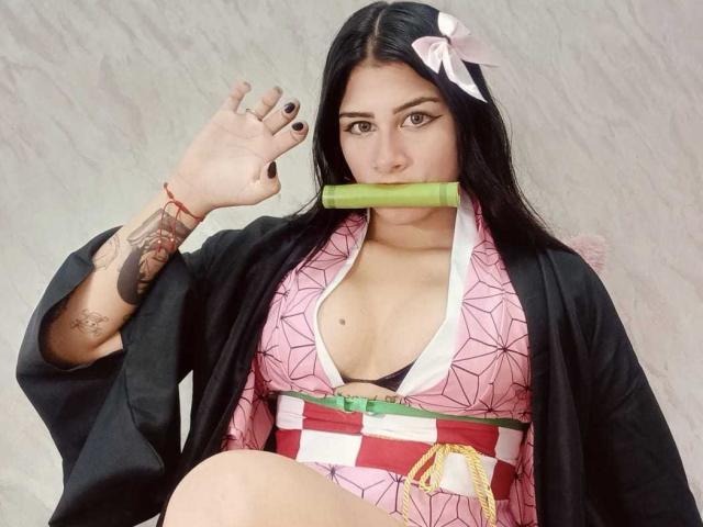BonnieGray with black hair, pink kimono, black robe, holding green bamboo, tattoos on right arm, black nails, pink bow, medium tits, white background, looking at camera.
