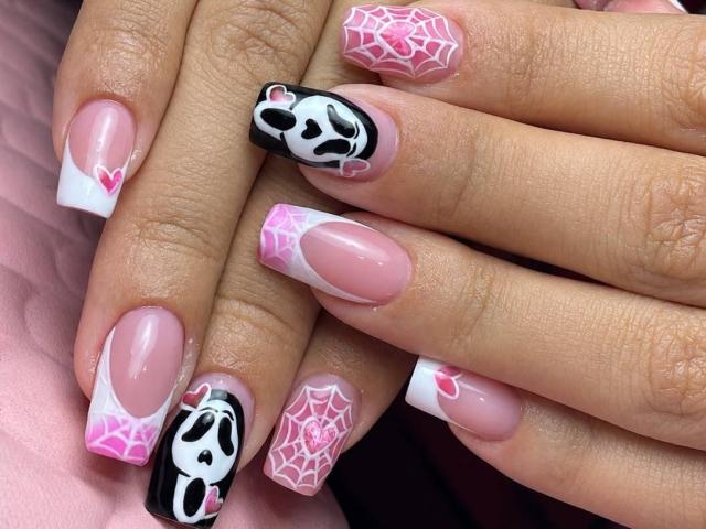 Les ongles d'EmmaWat sont peints avec des toiles d'araignées roses, des pointes blanches et des motifs de crânes noirs et roses sur des ongles roses brillants, mettant en valeur un nail art mignon, sexy et complexe..