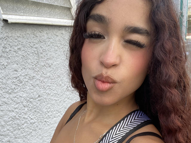 MadisonDawson's pouty lips are pressed together, her eyes are winking, and she has curly brown hair, wearing a black and white striped top. Her tits are small.