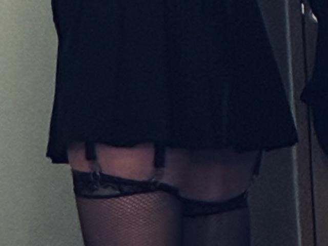 TifolyLaurent's black mini-skirt, showing black lace garter and fishnet stockings, with garter straps visible, focusing on her upper thighs and buttocks.