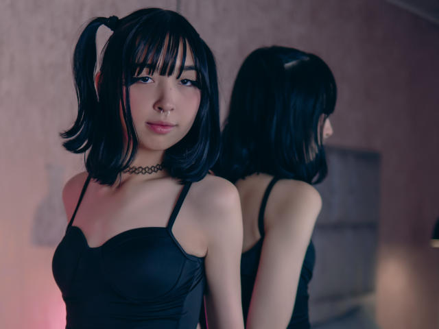 Vickmon with black pigtails, wearing a black choker and black tank top, showing small tits in a mirror reflection. Soft pink and purple lighting.