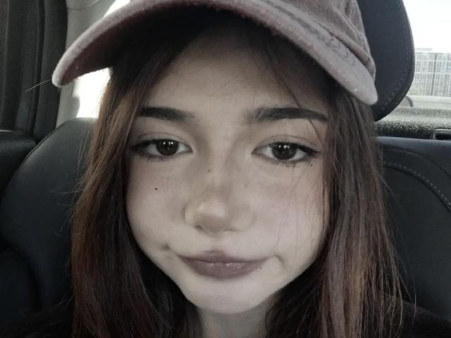 MarioChoudhary with brown eyes, wearing a pink cap, has light skin, small nose, and subtle smile. She's got a few moles on her face and brown straight hair.