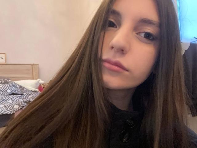 AleshiaFarman with long brown hair, light skin, and subtle makeup, wearing a black high-neck top, has a neutral expression, and is looking at the camera.
