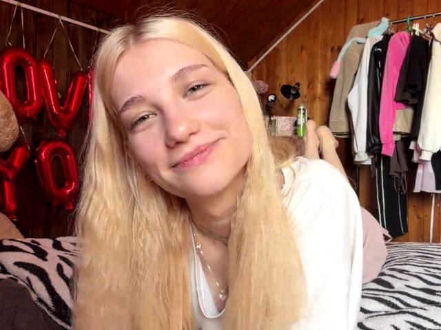 Georgann Whatcott hat blondes Haar, grüne Augen und ein leichtes Lächeln. Sie trägt ein weißes Hemd, und ihre kleinen Brüste sind kaum sichtbar. Sie lehnt sich auf einer Decke mit Zebra-Muster vor..