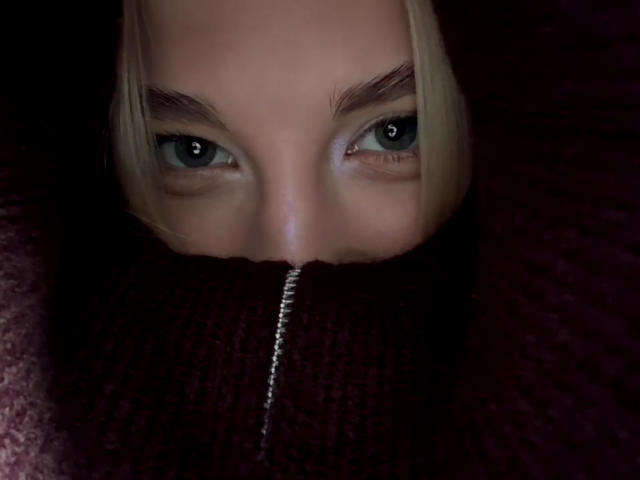 Los ojos azules de Georgann Whatcott miran fijamente hacia adelante, con el cabello rubio parcialmente visible, y lleva un pañuelo oscuro, acanalado y suave que le cubre la nariz y la boca..